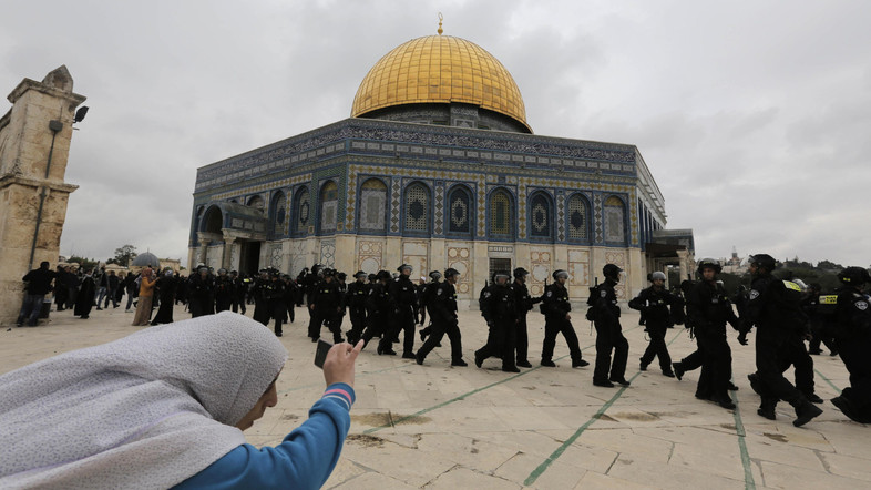 A Palestinian woman takes a picture as Israeli police walk in front of the Dome of the Rock during clashes with stone-throwing protesters in Jerusalem's Old City
